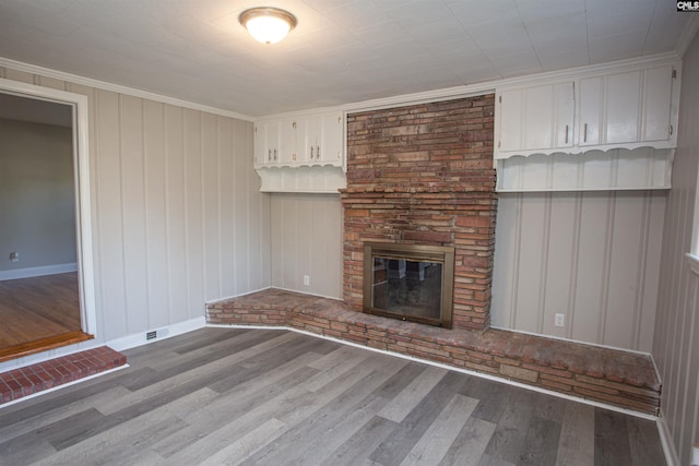 unfurnished living room with wood finished floors, ornamental molding, baseboards, and a large fireplace