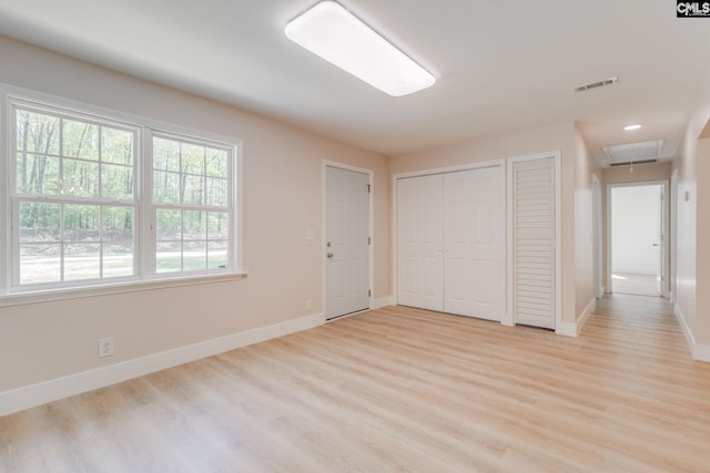unfurnished bedroom with light wood-type flooring, visible vents, attic access, multiple closets, and baseboards