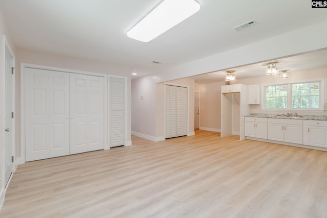 interior space featuring light wood-style floors, a sink, baseboards, and visible vents