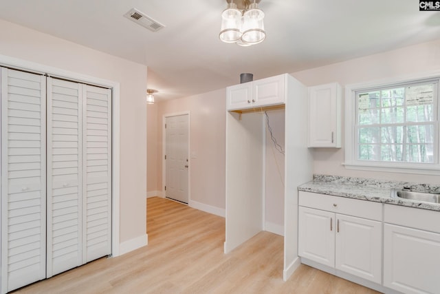 kitchen featuring visible vents, baseboards, white cabinetry, light wood-style flooring, and light stone counters