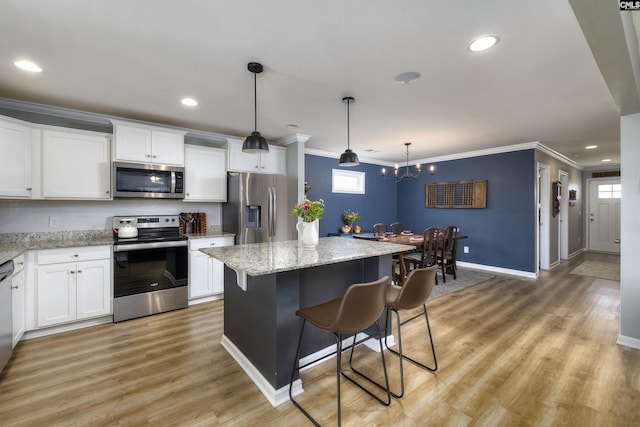 kitchen with a center island, white cabinets, appliances with stainless steel finishes, a kitchen breakfast bar, and crown molding