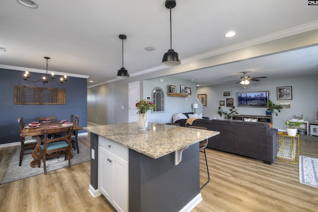 kitchen featuring hanging light fixtures, white cabinets, ornamental molding, light wood finished floors, and a kitchen island