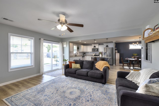 living area featuring light wood-style flooring, ceiling fan with notable chandelier, baseboards, and visible vents