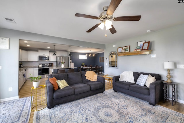 living area with light wood-style floors, ceiling fan with notable chandelier, visible vents, recessed lighting, and baseboards