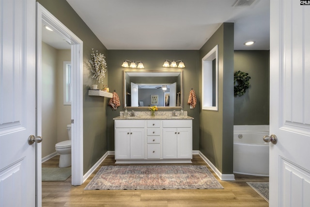 full bath with baseboards, toilet, double vanity, wood finished floors, and a garden tub