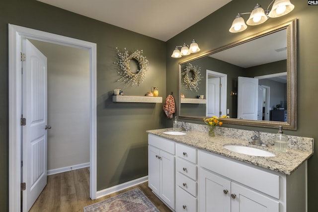 bathroom with a sink, baseboards, double vanity, and wood finished floors