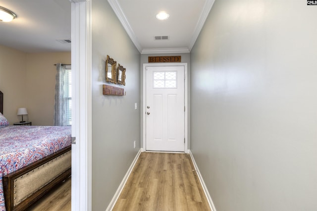 doorway with light wood-style flooring, baseboards, ornamental molding, and visible vents