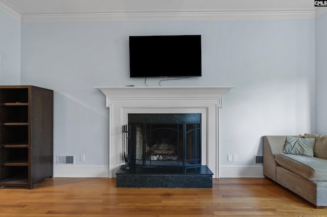 interior details with baseboards, crown molding, a fireplace with raised hearth, visible vents, and wood finished floors