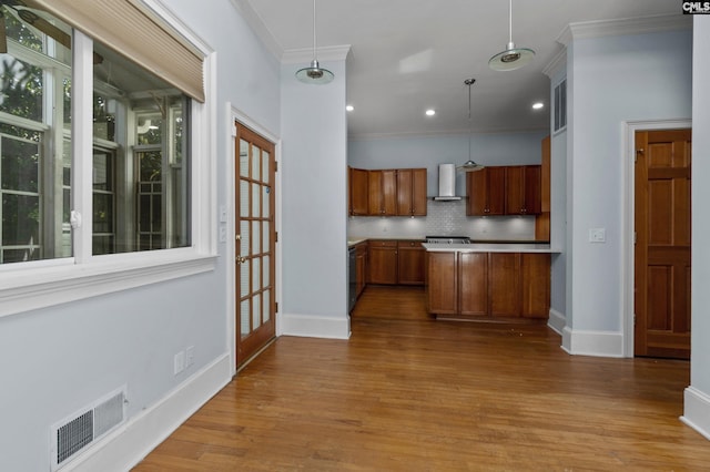 kitchen featuring wall chimney exhaust hood, tasteful backsplash, ornamental molding, visible vents, and brown cabinets