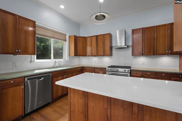 kitchen featuring crown molding, wall chimney range hood, light countertops, a sink, and stainless steel appliances