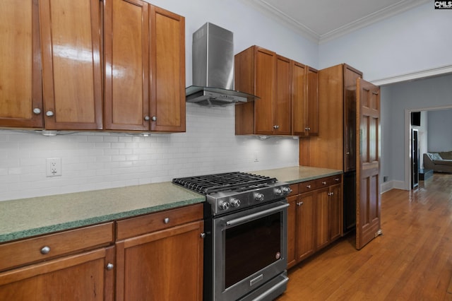 kitchen featuring wall chimney exhaust hood, ornamental molding, gas stove, brown cabinets, and light wood finished floors