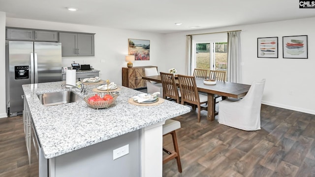 kitchen with a breakfast bar, stainless steel fridge, gray cabinetry, light stone countertops, and a sink