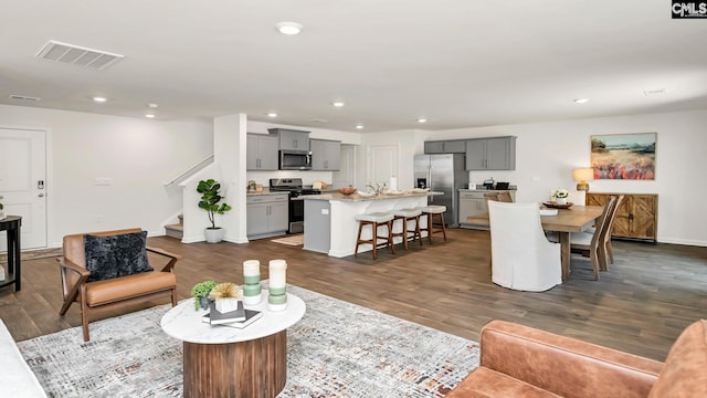 living area with dark wood-type flooring, visible vents, recessed lighting, and stairway