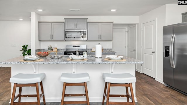 kitchen featuring visible vents, gray cabinets, light stone counters, stainless steel appliances, and a breakfast bar area
