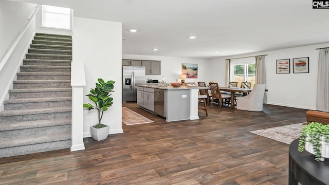 kitchen with an island with sink, recessed lighting, gray cabinets, dark wood-style flooring, and stainless steel appliances