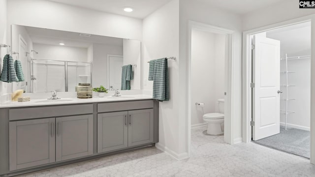 full bathroom featuring a shower stall, double vanity, a sink, and toilet