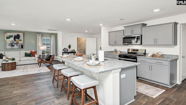kitchen featuring a breakfast bar, gray cabinets, light stone countertops, dark wood-type flooring, and stainless steel appliances