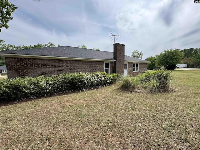 back of property featuring brick siding, a yard, and a chimney