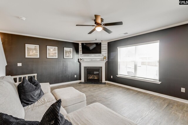 living room with baseboards, ornamental molding, a fireplace, a ceiling fan, and wood finished floors