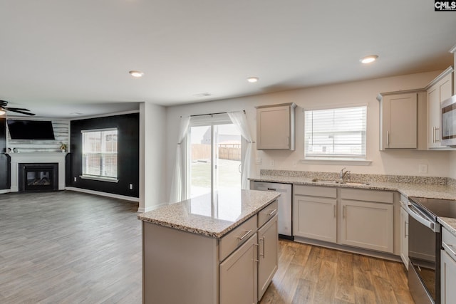 kitchen with a sink, appliances with stainless steel finishes, a ceiling fan, a fireplace, and light wood-style flooring