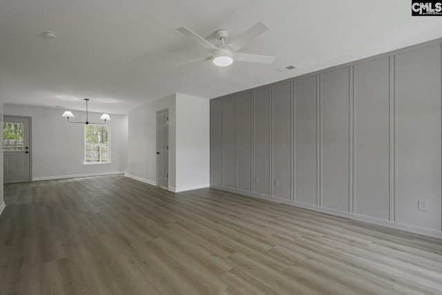 unfurnished living room featuring a decorative wall, visible vents, ceiling fan with notable chandelier, and wood finished floors