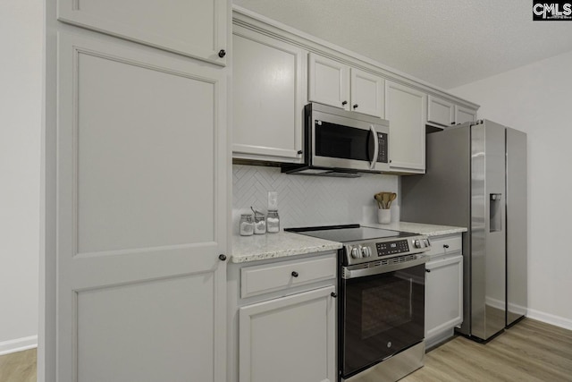 kitchen featuring stainless steel appliances, tasteful backsplash, light wood finished floors, and baseboards