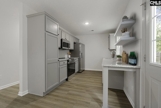 kitchen featuring stainless steel appliances, light wood-style flooring, a sink, and open shelves