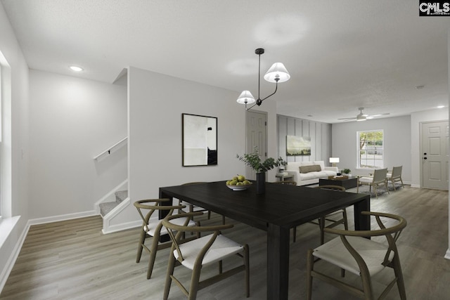dining area with stairs, light wood-style floors, baseboards, and a ceiling fan