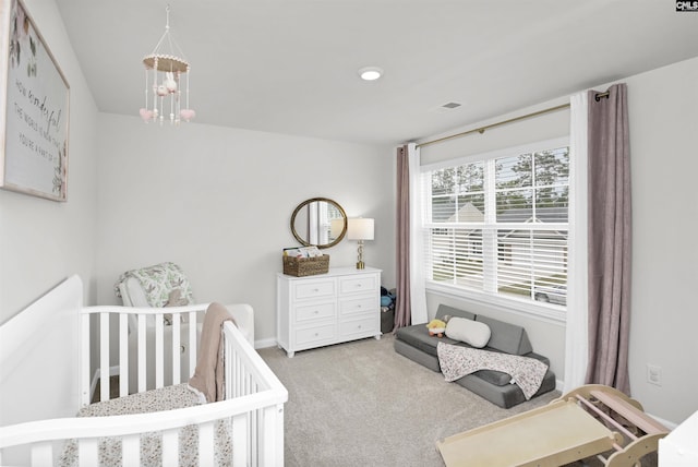 bedroom with light carpet, visible vents, an inviting chandelier, and a nursery area