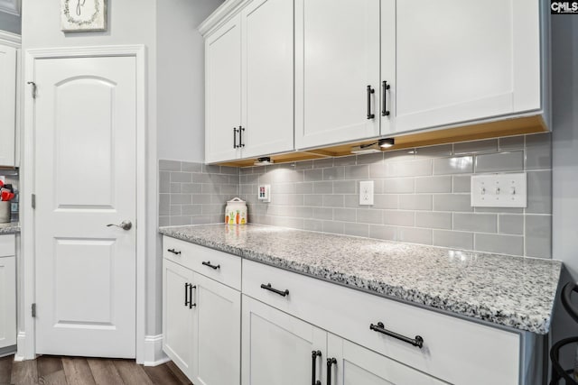 kitchen with white cabinets, light stone countertops, tasteful backsplash, and dark wood finished floors