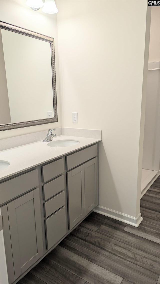 full bathroom with wood finished floors, double vanity, a sink, and baseboards