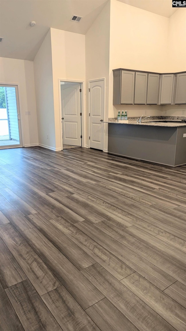 unfurnished living room with high vaulted ceiling, baseboards, dark wood-style floors, and visible vents