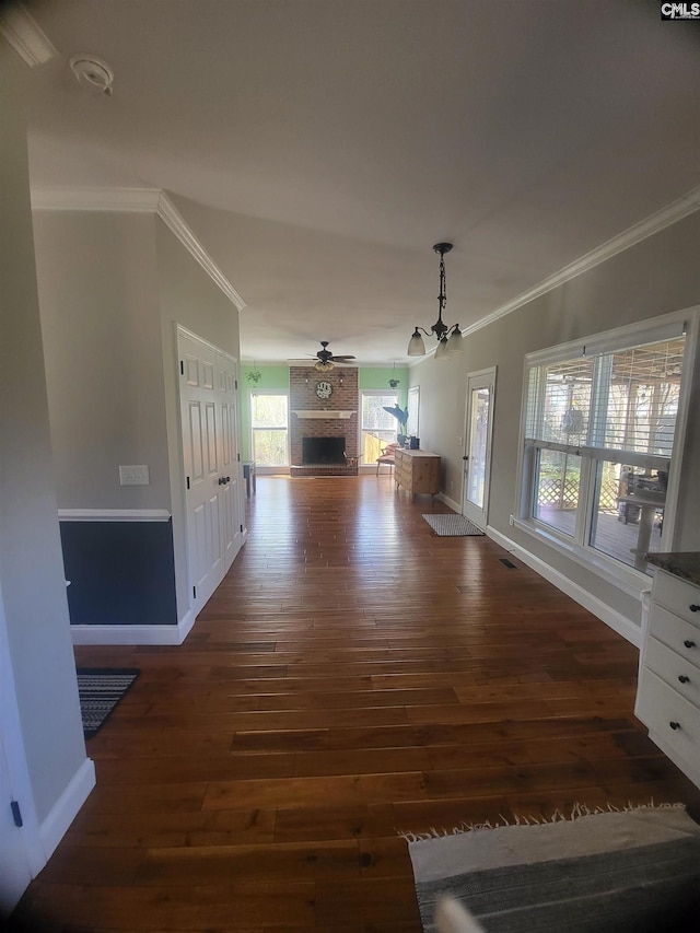 unfurnished dining area with dark wood finished floors, a brick fireplace, crown molding, and baseboards
