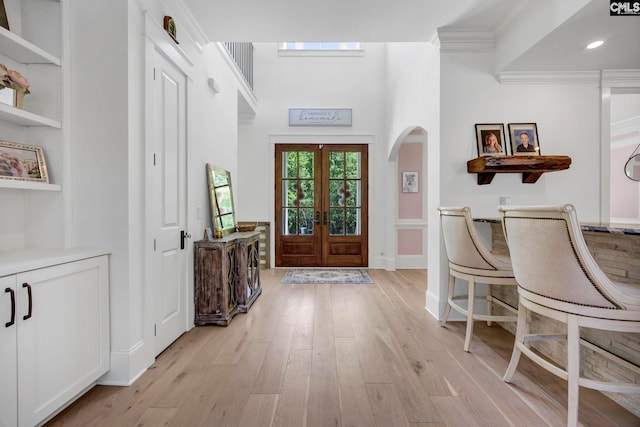 foyer with arched walkways, crown molding, french doors, and light wood-style flooring