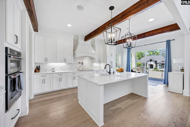 kitchen featuring stainless steel double oven, an inviting chandelier, premium range hood, beam ceiling, and tasteful backsplash