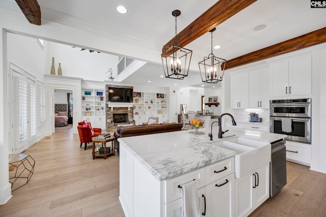 kitchen featuring a sink, light wood-type flooring, an inviting chandelier, beamed ceiling, and appliances with stainless steel finishes