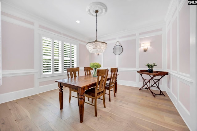dining room featuring a decorative wall, crown molding, a chandelier, and light wood-style flooring