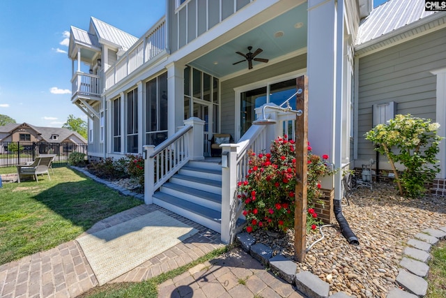 property entrance featuring fence, board and batten siding, ceiling fan, a lawn, and metal roof