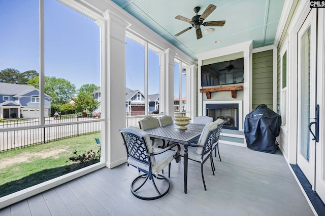 sunroom featuring a ceiling fan, outdoor dining space, and a fireplace