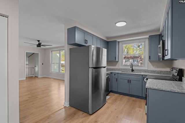 kitchen with stainless steel appliances, a sink, light wood-type flooring, a ceiling fan, and light stone counters
