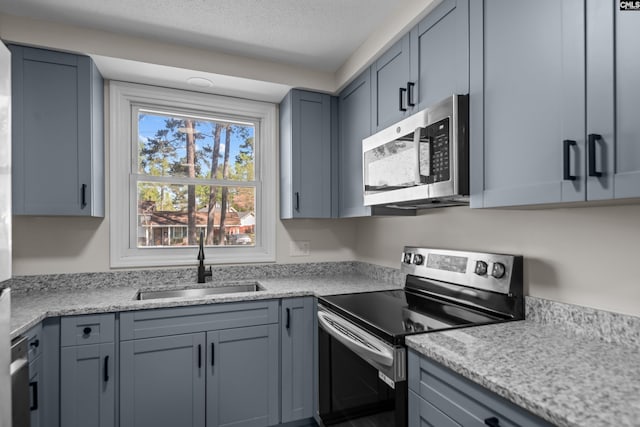 kitchen with gray cabinetry, a sink, a textured ceiling, and appliances with stainless steel finishes
