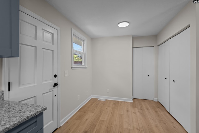 doorway with light wood-type flooring, visible vents, and baseboards