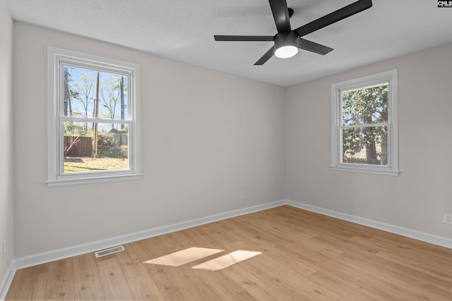 empty room featuring light wood-style flooring, visible vents, and a wealth of natural light