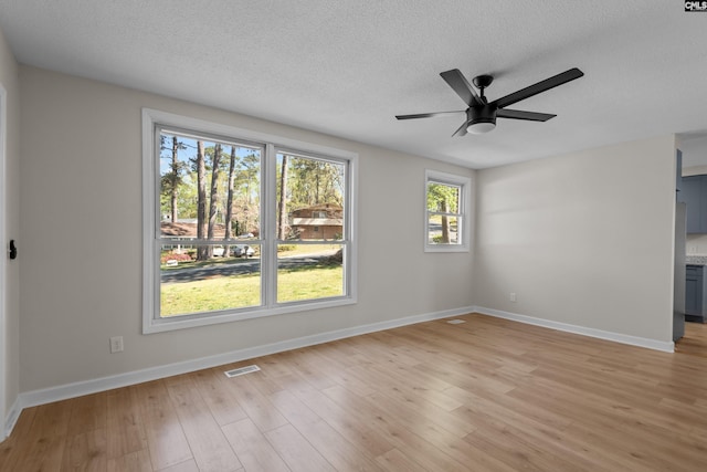 unfurnished room with a textured ceiling, light wood-style floors, ceiling fan, baseboards, and visible vents
