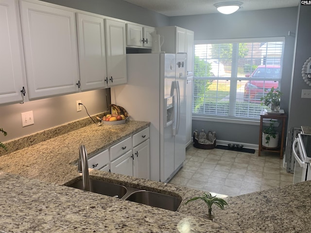 kitchen featuring white cabinets, light stone counters, a sink, and white appliances