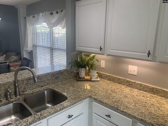 interior details with white cabinets, light stone counters, and a sink