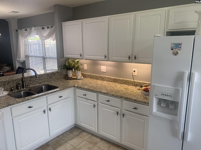 kitchen with white fridge with ice dispenser, light stone countertops, white cabinetry, and a sink