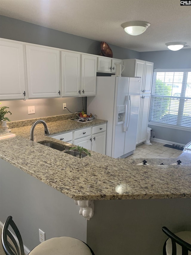 kitchen featuring light stone counters, a sink, white fridge with ice dispenser, baseboards, and white cabinetry