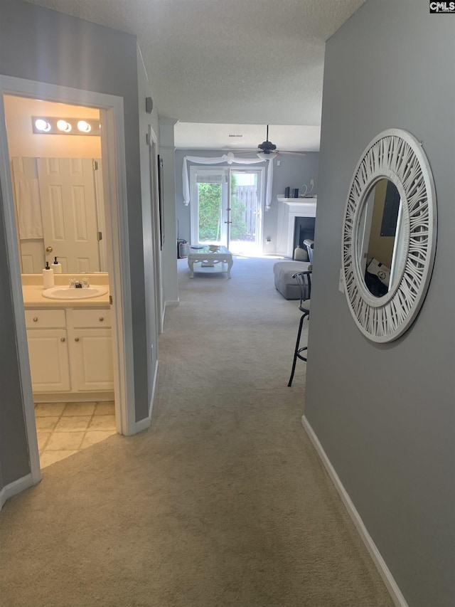 corridor featuring a textured ceiling, baseboards, light carpet, and a sink