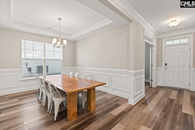 dining space with a chandelier, a raised ceiling, wood finished floors, and visible vents